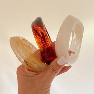 Detailed view of three chunky resin bangles in amber, cream, and marble patterns