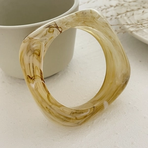 Detail of chunky amber acrylic bracelet with marble pattern on a white table