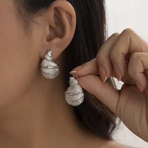 Silver conch shell drop earrings with horizontal ribbed texture shown on model and hand