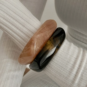 Close-up of translucent amber and dark brown chunky acrylic bangles with marble texture