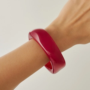 Detailed view of a thick translucent rose red acrylic geometric bangle on a wrist