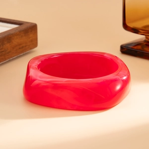 Macro shot of a red marbled acrylic bangle on a minimalist cream-colored surface