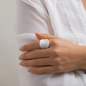 Detail of silver textured wide band ring with vertical pleated pattern on a finger
