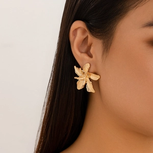 Close-up of a large gold floral earring with a brushed metal texture worn by a model
