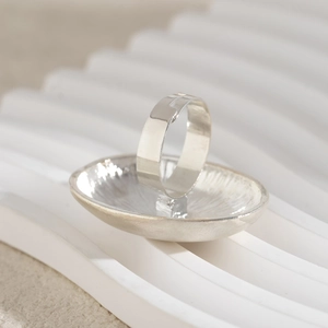 Macro detail of silver pleated metal ring with radial hammer texture on a white stand