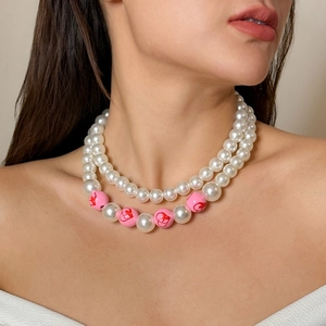 Detailaufnahme einer geschichteten Perlenkette mit rosa Perlen an einem Model