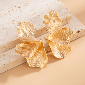 Detailopname van grote gouden ginkgoblad oorbellen met textuur op natuursteen