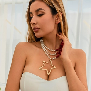 Detail van gelaagde parelketting met een grote gehamerde gouden ster hanger aan de ketting