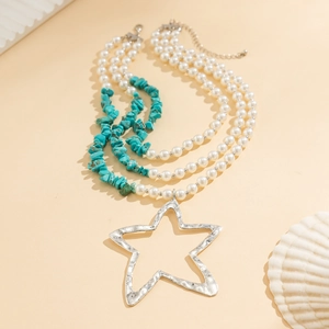 Detail van gelaagde ketting met parels, blauwe stenen en een zilveren sterhanger
