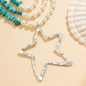 Gelaagde bohemian sterrenketting met parels en turquoise stenen op zandige achtergrond