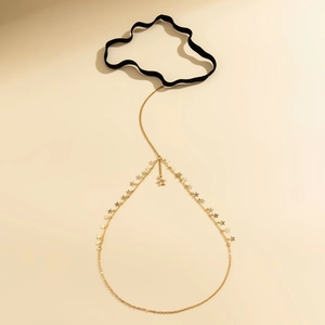 Detail of star charm leg chain with golden fringe and black elastic band on beige background