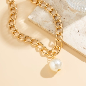 Detail of chunky gold chain link necklace featuring a large white round pearl pendant