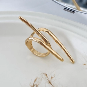Macro view of gold minimalist bow ring on white ceramic tray with herb accents