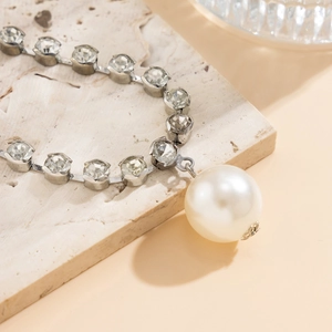 Close-up of gothic layered necklace featuring silver metal, crystals, and a large pearl pendant