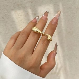 Detailed close-up of golden metallic liquid-shaped double ring worn on a hand