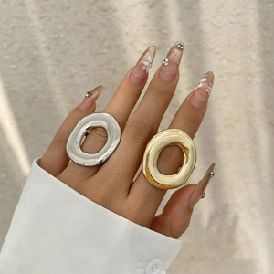 Detail shot of large oval hollow metal rings in gold and silver finish on hand