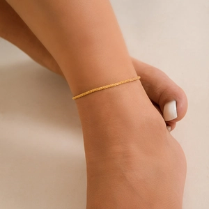 Detailed close-up of textured gold anklet chain on ankle with shimmering minimalist design
