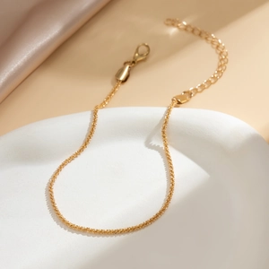 Close-up of gold layered anklet with lobster clasp on ceramic plate detail