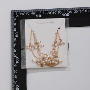 Détail d'un collier à pompon en perles avec chaînes dorées et perles blanches et mètre