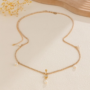 Detalle de cadena de cuerpo dorada con diamantes de imitación, perlas y colgante redondo