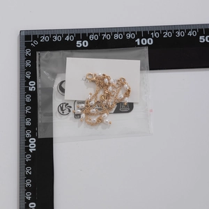 Détail d'un collier de perles dorées avec fermoir mousqueton mesuré sur une règle