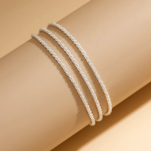 Detail view of shimmering silver layered ankle chains with fine bead and twisted rope texture