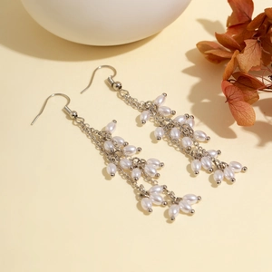 Vue détaillée de boucles d'oreilles à pompons argentés et perles de riz sur fond beige