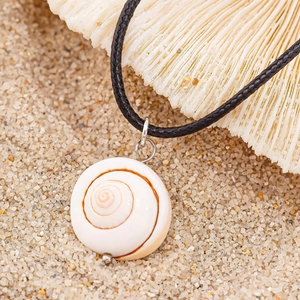 Close-up of a natural white spiral shell pendant on a black woven cord with beach background
