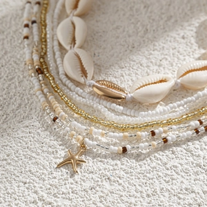 Detail van de lichaamsketting met gouden zeester en witte schelpen op wit zandstrand