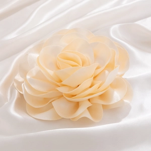 Detail of multi-layered apricot fabric rose brooch with silk petals on white satin background