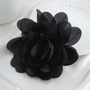 Detail einer mehrlagigen schwarzen Stoffblumen-Brosche mit Satinblüten auf Keramik
