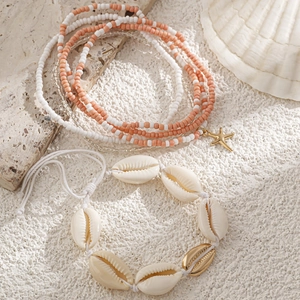 Detail van strandlichaamsketting met natuurlijke schelpen en gouden zeester op wit zand