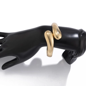 Detailansicht des polierten goldenen Tropfen-Armreifs auf einem schwarzen Handmodell