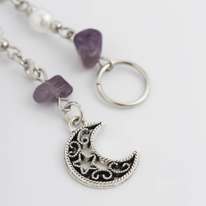 Dettaglio di pendente a luna d'argento con pietre naturali viola e una perla bianca