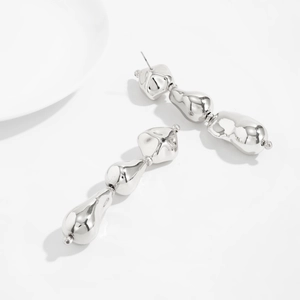 Détail macro de boucles d'oreilles en métal liquide argenté au fini poli miroir