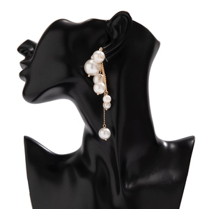 Détail de boucles d'oreilles pampilles avec perles blanches et chaîne dorée sur buste noir