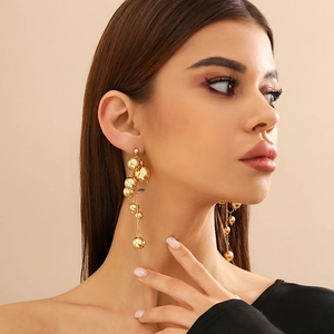 Détail de boucles d'oreilles dorées à pampilles de perles portées par un mannequin
