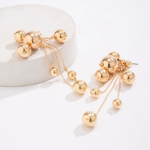 Détail de boucles d'oreilles boules dorées CCB avec franges de perles sur socle gris