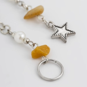 Dettaglio di ciondolo a stella e pietre gialle su accessorio con catena d'argento e perla