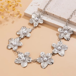 Detail of silver body chain featuring pearl flower charms on a textured stone background