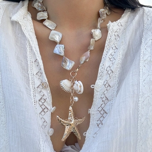 Primo piano di una collana bohémien con conchiglie, stella marina dorata e perla su modella