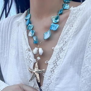 Dettaglio collana con conchiglie blu e ciondolo a stella marina dorata su pizzo bianco