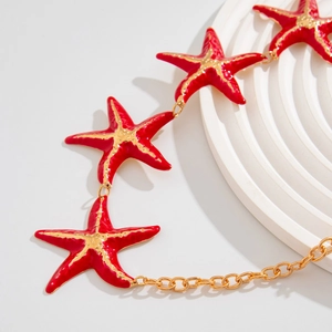 Detail of gold chain body jewelry featuring red starfish pendants with enamel finish