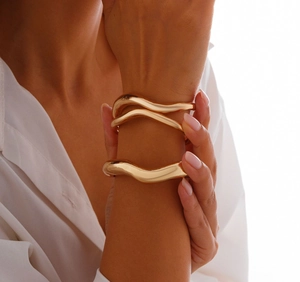 Dettaglio di due bracciali rigidi dorati ondulati irregolari per un look moderno a strati
