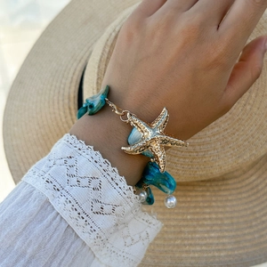 Dettaglio collana con stella marina dorata, pietre blu e perle su maniche di pizzo bianco