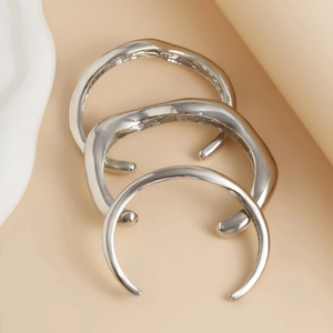 Dettaglio di tre bracciali rigidi impilabili color argento con texture effetto lava