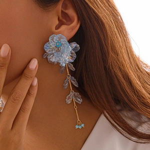 Détail de boucles d'oreilles fleurs bleu clair irisées avec accents en métal doré