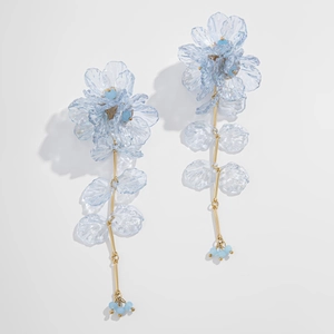 Détail des boucles d'oreilles fleurs bleues translucides avec tiges dorées et glands