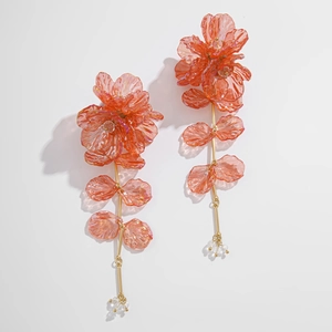 Détail de boucles d'oreilles pendantes fleurs avec pétales irisés rose-orange et tige or