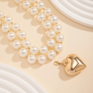 Detailed macro view of double-layer pearl necklace with a polished gold heart pendant